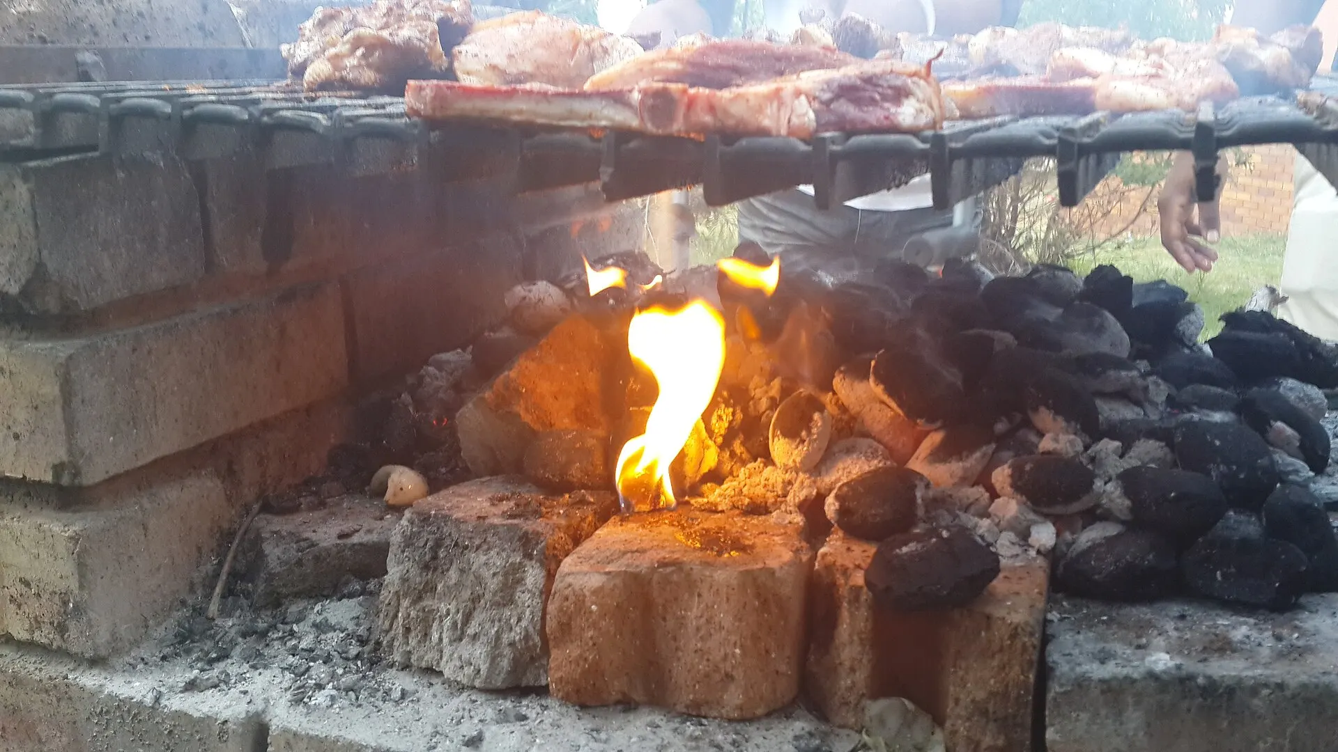 Burnt-down coals with a layer of grey ash beneath a braai grid